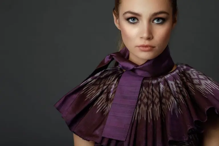 Close-up view of purple Thai silk couture cocktail dress showing pleated collar with patterned edge, detachable bow, and upper part of the knee-length silhouette, by Saskia ter Welle