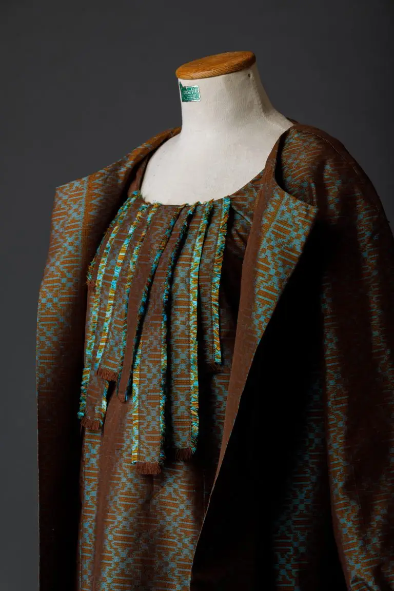 Studio mannequin displaying brown and green couture ensemble with silk dress, matching coat and silk-covered pumps, designed by Saskia ter Welle