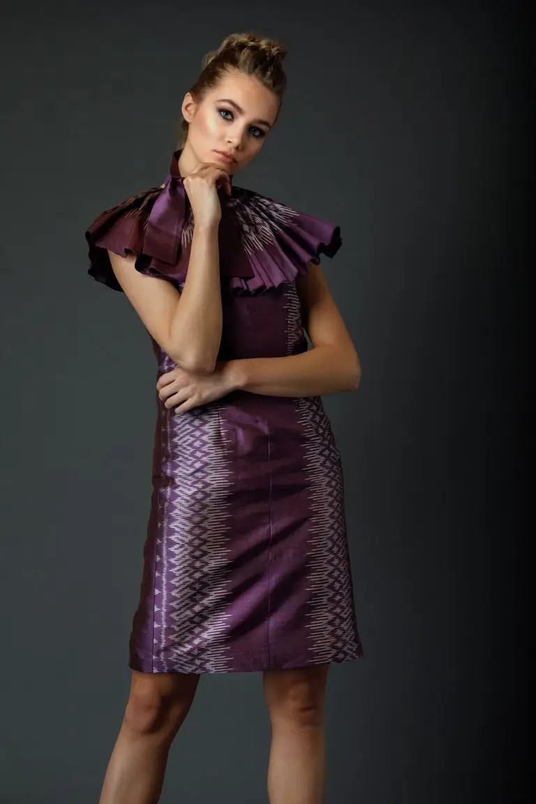 Model in purple Thai silk couture dress with pleated collar and patterned edge, captured in a reflective pose, by Saskia ter Welle