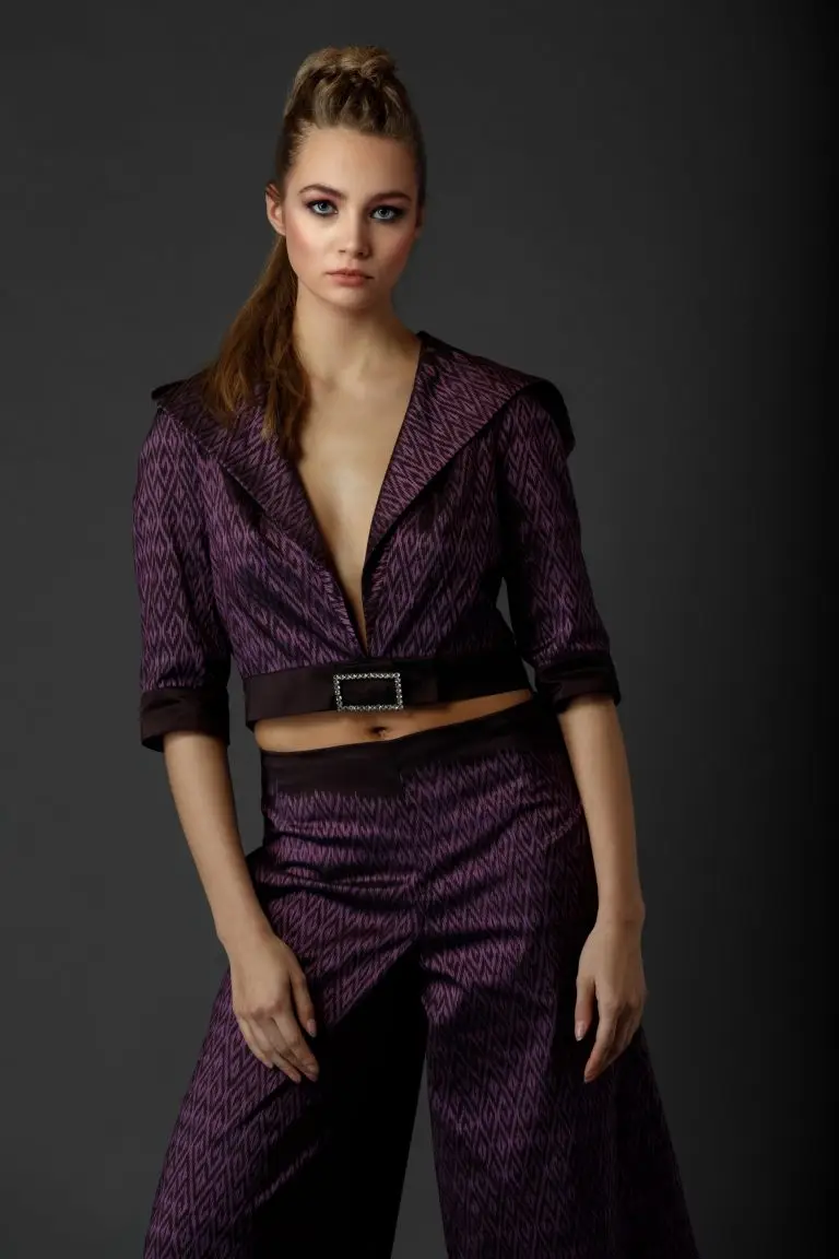 Front view of purple Thai silk couture suit with woven pattern, featuring cropped wide-leg trousers and short hooded jacket with deep neckline, by Saskia ter Welle