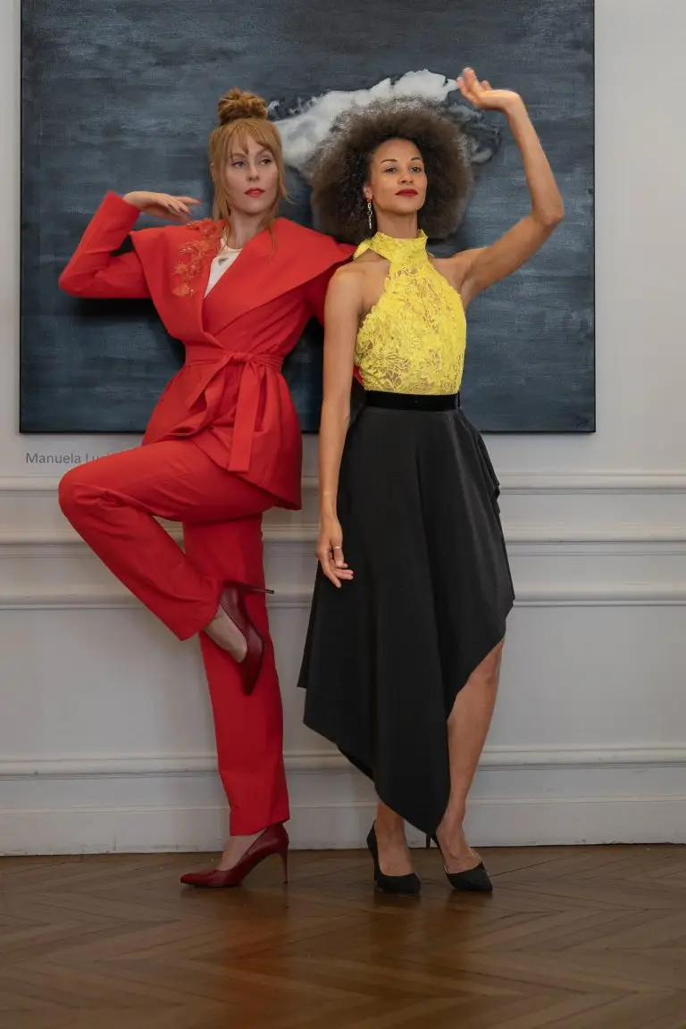 Two dancers performing at the opening of the Pop Up exhibition in Paris, wearing couture outfits by Saskia ter Welle: an orange trouser suit with embroidered collar and a black-and-yellow lace ensemble