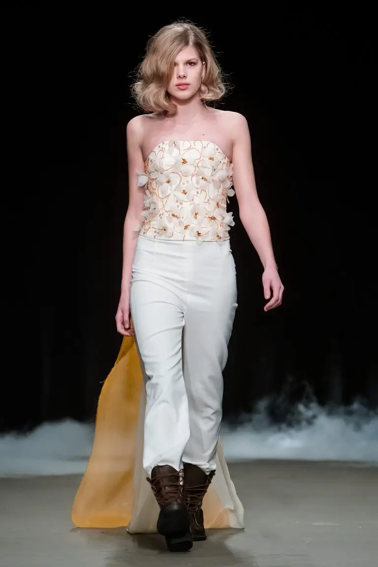Couture bridal finale look at Amsterdam Fashion Week: off-white high-waisted trousers with hand-embroidered corset of silk organza flowers and a flowing train in off-white and orange, by Saskia ter Welle