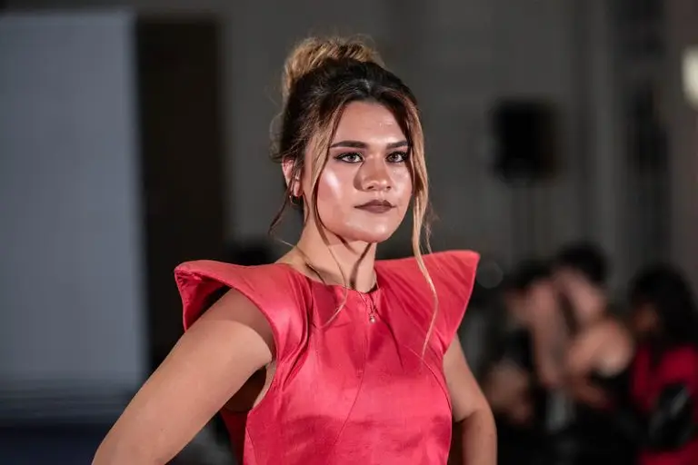 Model wearing a coral-red dress in handwoven Thai silk with a sharp shoulder line and sculpted silhouette, designed by Saskia ter Welle.