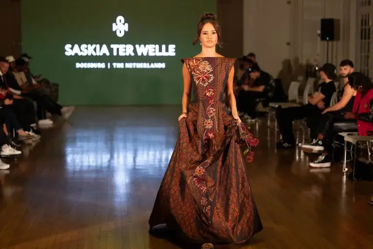 Model on the runway in a deep brown-bordeaux evening gown of handwoven Thai silk with woven motifs and couture embroidery combining broderie d’art and Al Aire techniques.